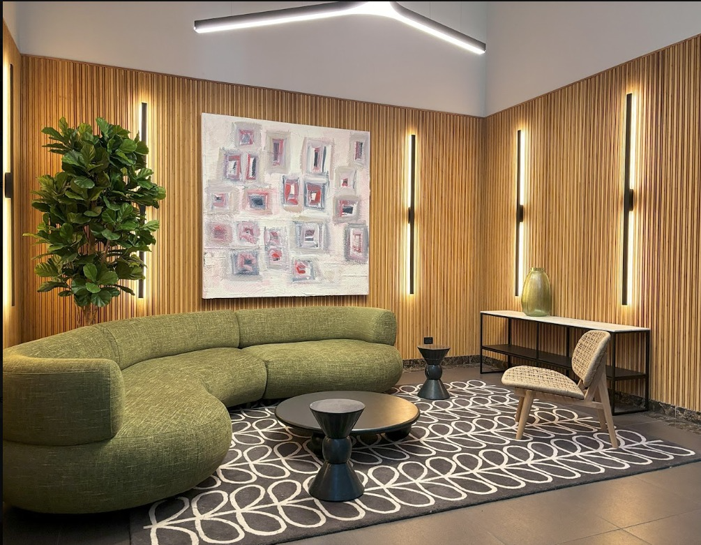 A lobby lounge lined floor to ceiling with vertical bamboo battens, with a curved green sofa and softly lit wall panels