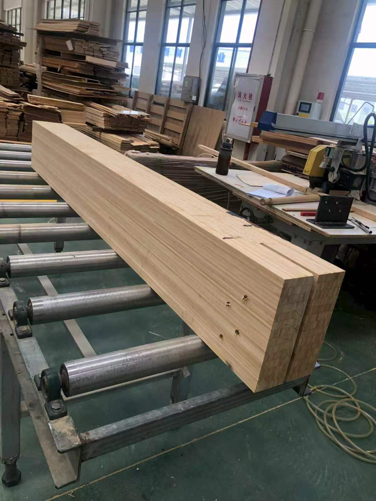 A finished laminated engineered bamboo beam on roller conveyors in a manufacturing plant