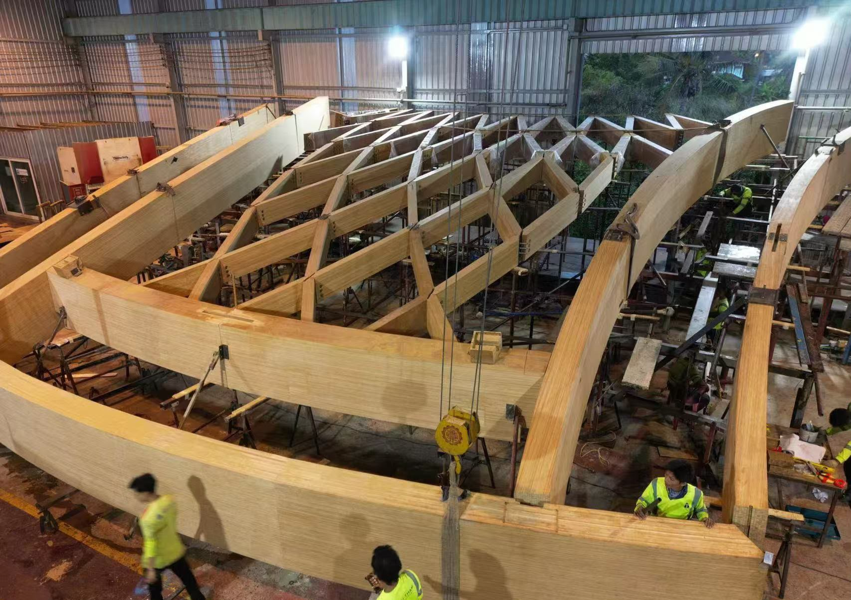 Curved engineered bamboo arches and beams being assembled into a structural frame in a fabrication shop